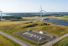 EBRD to Advance Energy with Eesti Energia First Green Bond Aerial view of a renewable energy site with wind turbines, solar panels, and a utility area in a rural landscape within reach of water in the distance.