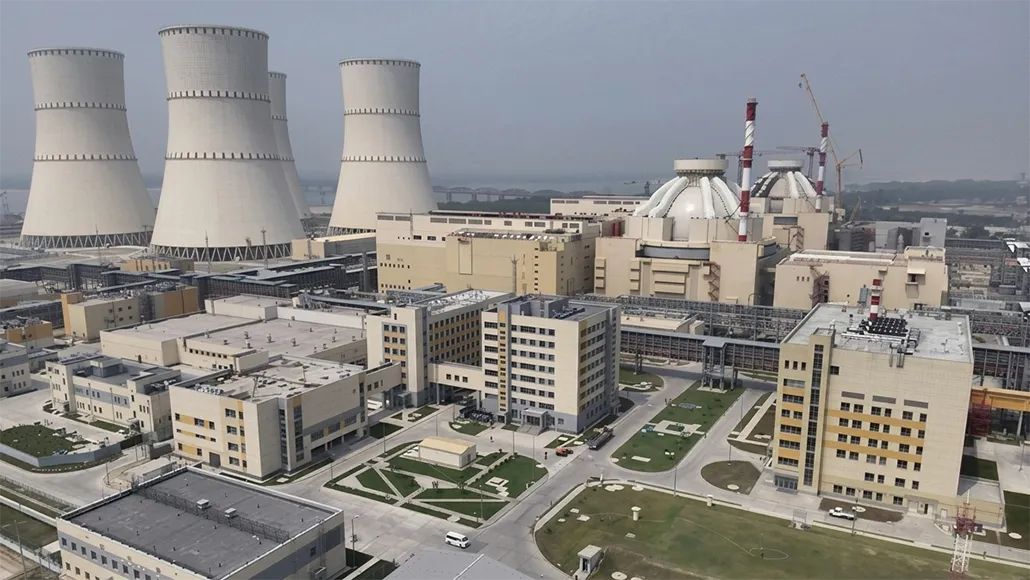Bird's-eye view of a nuclear power plant with four large cooling towers and beige office buildings in the foreground