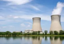 Canada Plans New Nuclear Energy Strategy for Nuclear Growth Two large cooling towers at a power plant along a calm river, with steam rising and a blue sky above.