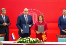 North Macedonia and Croatia Forge Energy Cooperation Pact Officials at a signing ceremony holding blue and gray folders, with Croatian and North Macedonian flags on the table, against a red backdrop.