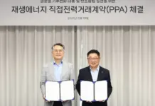 Cosmax Boosts Sustainability with Hanwha Solutions Solar PPA Two men in suits hold open signed documents at a renewable energy PPA signing ceremony, with a banner in Korean above them.