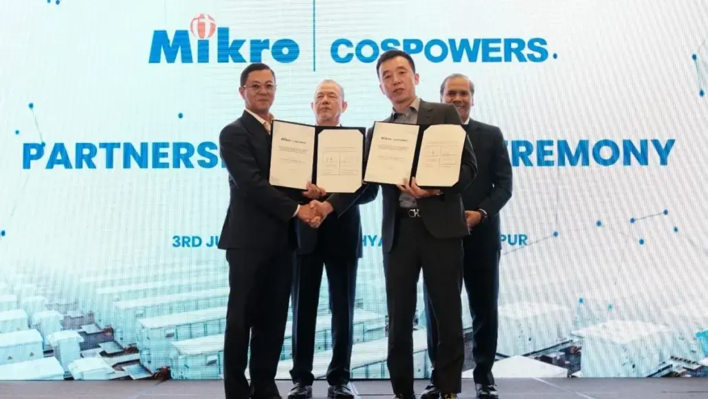 Four men in suits on a stage hold open signed documents and shake hands during a partnership ceremony, with a blue backdrop reading 'Mikro' and 'PARTNERSHIP CEREMONY'.