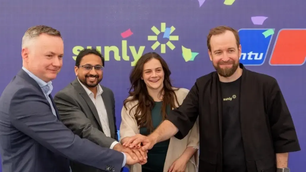 Four professionals join hands in a circle, smiling, with a Sunly-branded backdrop behind them.