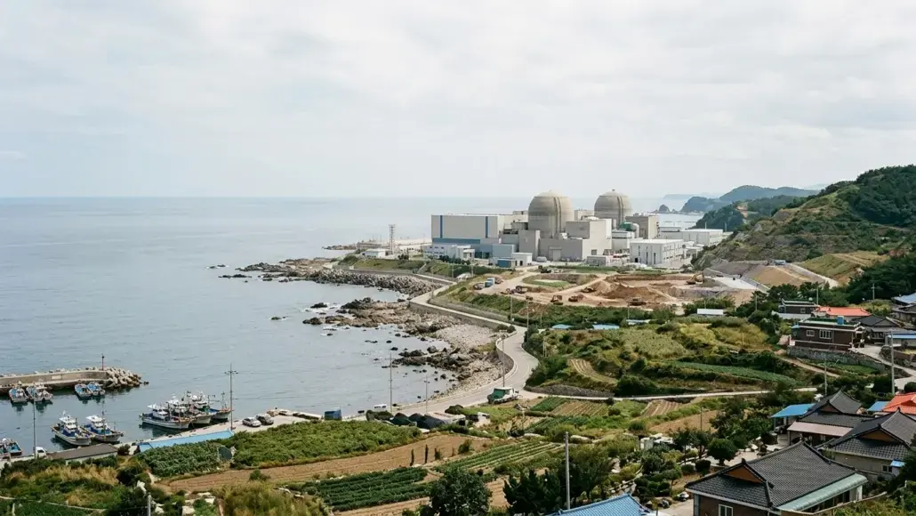 Coastal nuclear power plant with two domed cooling towers near the sea and harbor in front.