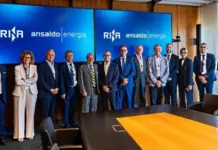 Nuclear Supply Chain Gains Support through Italy Initiative Group of professionals in business attire posing for a photo in a conference room in front of two large screens displaying 'RINA' and 'ansaldo energia' logos.