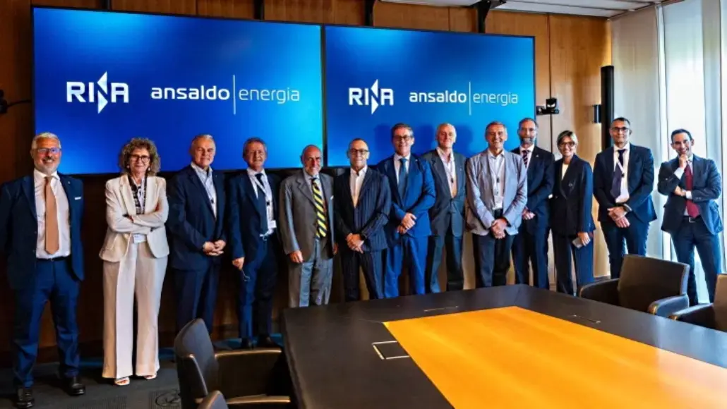 Group of professionals in business attire posing for a photo in a conference room in front of two large screens displaying 'RINA' and 'ansaldo energia' logos.