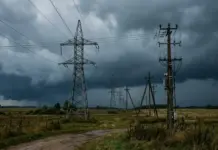 Lithuania and Latvia Sign Electricity Network Support Deal Transmission towers and power lines stretch across a rural field under dark storm clouds as a storm approaches.