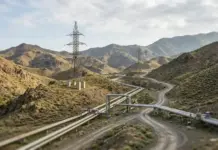 Iran and Armenia Strengthen Strategic Energy Cooperation Roadmap Desert hills with elevated pipelines and metal transmission towers traversing winding dirt roads under a cloudy sky