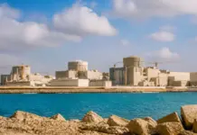 Egypt, Rosatom Discuss Dabaa Nuclear Power Plant and SMRs Beige industrial complex under construction along a rocky shoreline, with cranes and calm blue water in front.