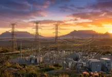DBSA, NTCSA Partner Up to Boost South Africa Grid Expansion Electrical substation with tall transmission towers and power lines across a desert landscape at sunset.