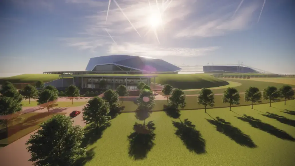 Wide view of a futuristic building with a curved glass roof, surrounded by lawns, trees, and a bright sunlit sky.