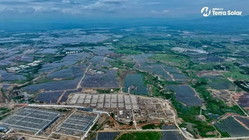 Aerial view of a vast solar farm with rows of panels across green countryside; Terra Solar logo in the corner of the image.