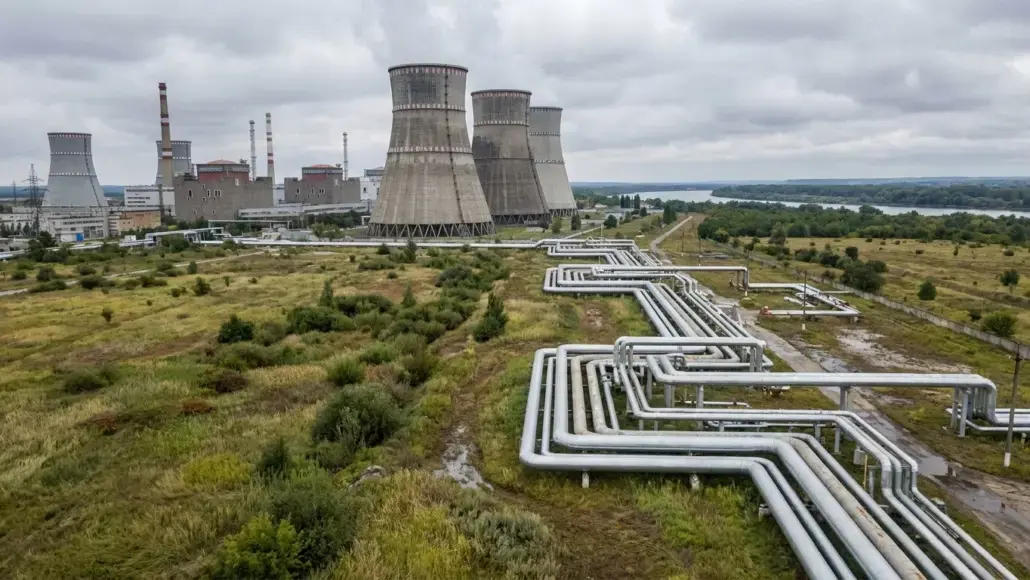 Industrial power plant with large cooling towers and extensive above-ground piping in a flat, rural landscape.